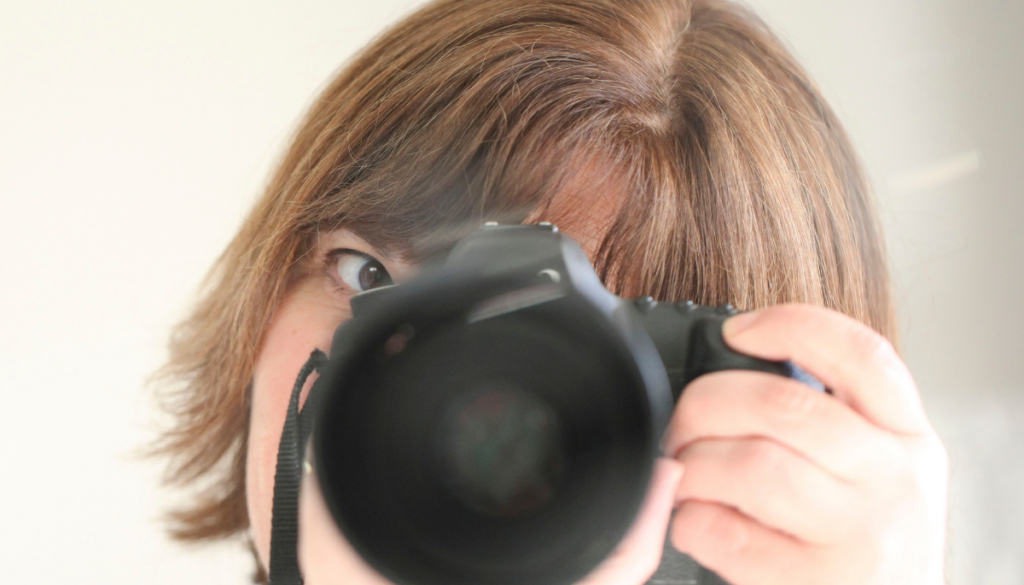 Michelle holding a camera and looking through the viewfinder, reflecting her love of photography and everyday storytelling.