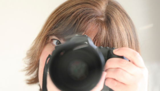 Michelle holding a camera and looking through the viewfinder, reflecting her love of photography and everyday storytelling.